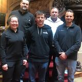 Gruppe der Absolvent*innen und zwei Prüfer vor einer wunderschönen gedrechselten Holzstiege